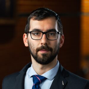 Portrait of Diego Cerrai, wearing a dark suit, light blue collared shirt and a dark blue tie.