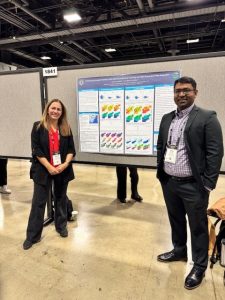 Marina Astitha (left) and a colleague pose in front of a colorful research poster at a professional conference.