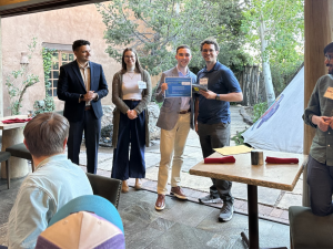 Image of Samuel Rothfarb receiving the NVIDIA GPU Award during an outdoor ceremony. He is smiling and holding a certificate while standing next to an event organizer. Three other attendees are standing nearby, applauding.